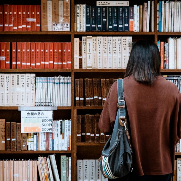 woman wearing brown shirt carrying black leather bag on front of library books