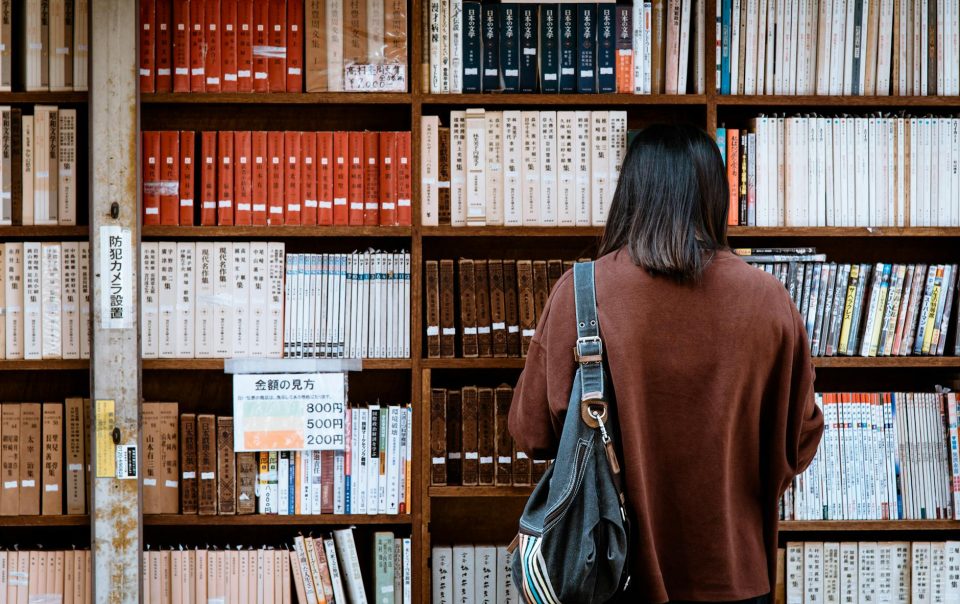 woman wearing brown shirt carrying black leather bag on front of library books